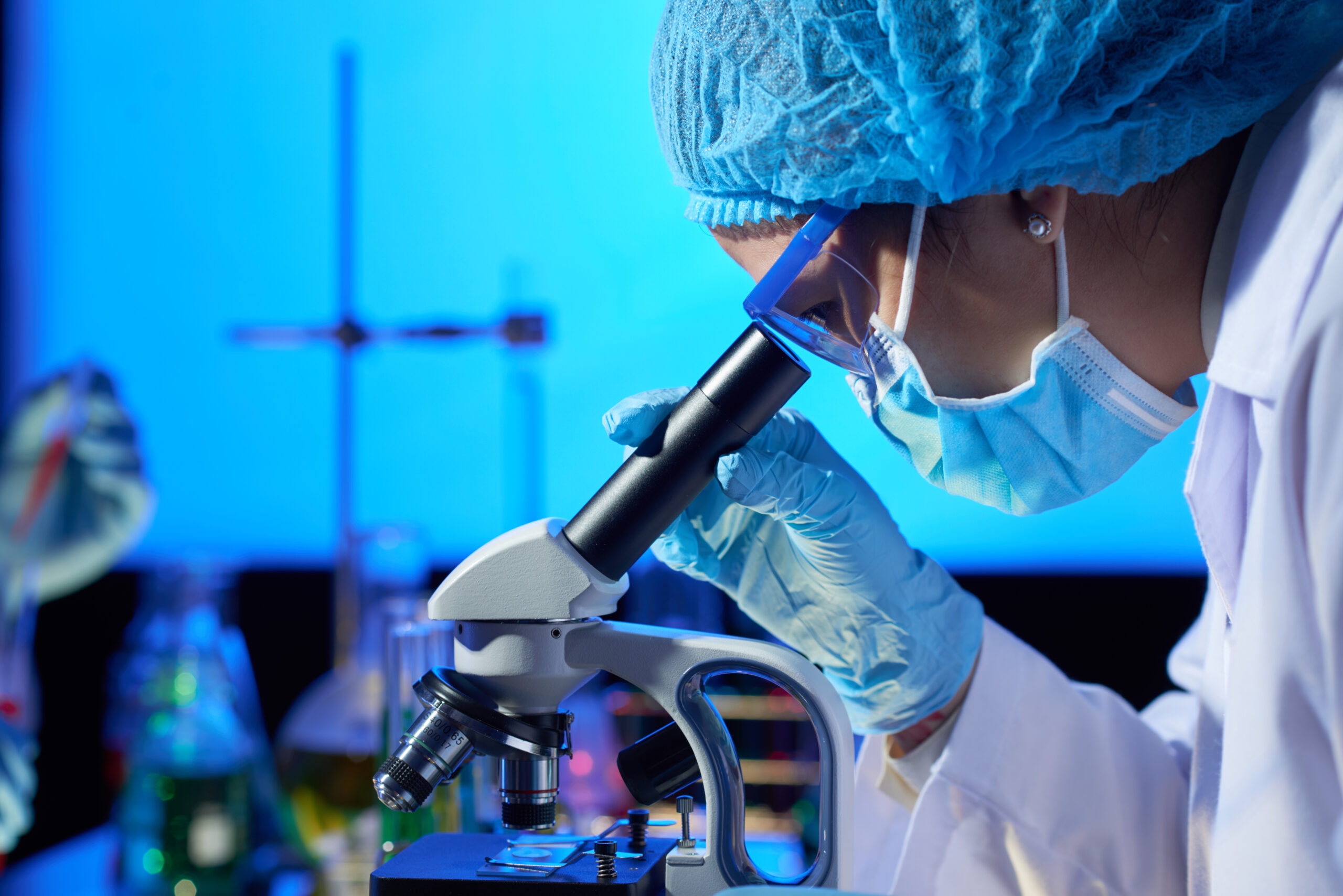 Profile view of concentrated Asian microbiologist examining sample with help of modern microscope while wrapped up in work at dim laboratory